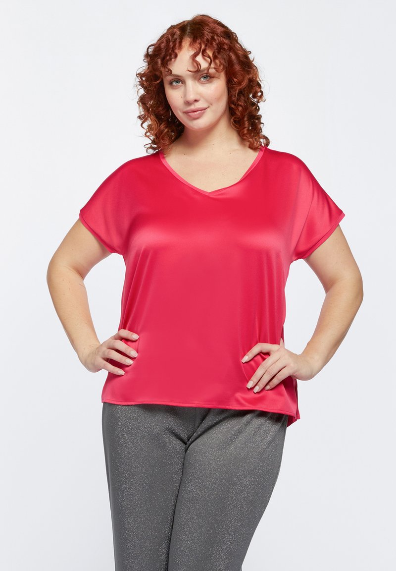 Blusa rossa a scollo a V con maniche corte, realizzata in un tessuto liscio e lucido. Abbinata a pantaloni grigi scintillanti. Design semplice, senza fantasie o dettagli.