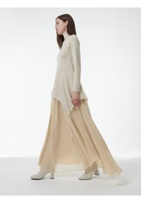 Beige lange mouw top met een hoge hals, gecombineerd met een vloeiende beige maxi rok. Glad, lichtgewicht materiaal; hoge, lichtgekleurde hakken.