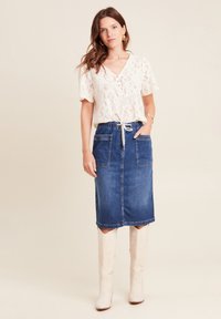 Top in pizzo a maniche corte color crema con bottoni, abbinato a una gonna midi in denim blu con tasche frontali e vita regolabile con cordoncino. Stivali bianchi.