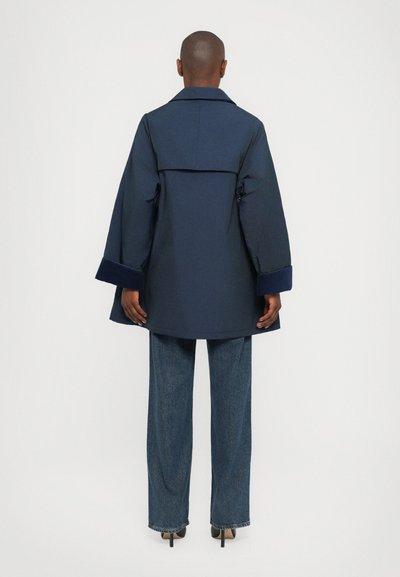 Navy blue coat with a wide collar, bell sleeves, and a back yoke detail, paired with high-waisted denim pants and pointed heels.