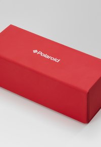 Boîte rectangulaire rouge avec une texture lisse, arborant un logo Polaroid blanc à l'avant. AUCUN motif ou matériel notable visible.
