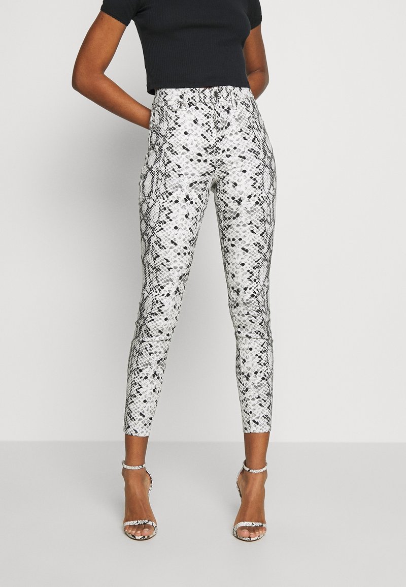 Personne portant un pantalon taille haute, fuselé, à imprimé serpent, avec des talons à bride à la cheville assortis, associés à un haut noir à manches courtes.
