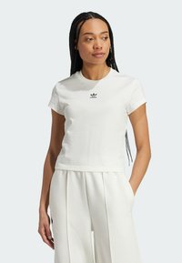 Biała, krótko rękawowa koszulka z bawełny z okrągłym dekoltem i małym czarnym logo Adidasa na piersi, zestawiona z białymi plisowanymi spodniami.
