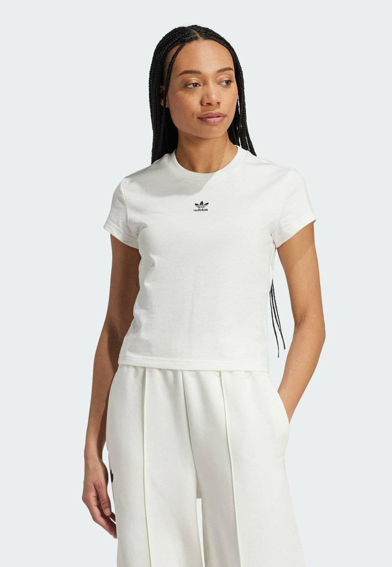 Biała, krótko rękawowa koszulka z bawełny z okrągłym dekoltem i małym czarnym logo Adidasa na piersi, zestawiona z białymi plisowanymi spodniami.