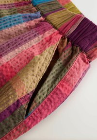 Close-up van kleurrijke gestreepte stof met geplooide stiksel en een open zijnaadzak op een witte achtergrond.