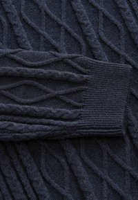 Granatowy sweter z dzianiny z wypukłym wzorem diamentów i ściągaczami. Miękka tekstura i skomplikowane detale warkoczowe na całej powierzchni.