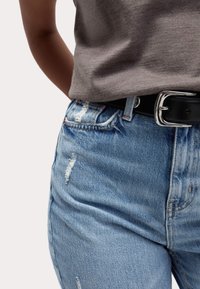 Verwaschene hellblaue Jeans im High-Waist-Schnitt, kombiniert mit einem grauen, kurzärmligen, taillierten Oberteil und einem schwarzen Gürtel mit einer silbernen Schnalle.