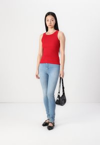 Rød tætsiddende tanktop, lyseblå skinny jeans, sort håndtaske og sorte flade sko med sølvdetaljer. Glat stof og strømlinet silhuet.