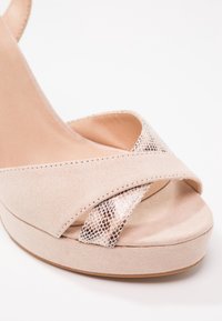 Sandale compensée en daim beige avec un design croisé et un accent texturé à imprimé serpent sur la partie supérieure. Doublure intérieure douce. Semelle plate à plateforme.