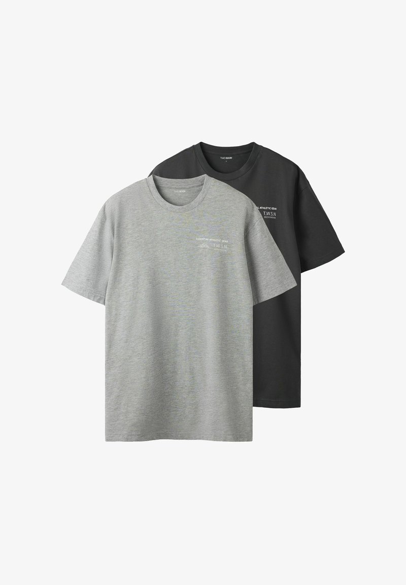 Deux T-shirts à col rond, un gris et un noir, en coton doux. Chaque T-shirt présente un petit logo blanc sur le côté gauche à l'avant.