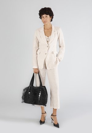 Stribet beige blazer og bukser med dobbeltknapper; sort vævet taske med frynser og store knapper; spidse sorte hæle.