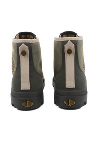 Botas de tornozelo em tela verde com detalhes bege, apresentando um logótipo circular, ferragens metálicas e solas de borracha texturizadas. Marca PALLADIUM visível.