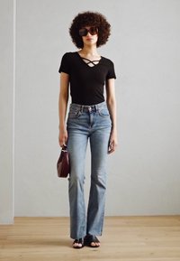 Svart tettsittende topp med krysslinning, lyseblå flared jeans, svarte åpne sandaler, og en liten burgunder håndveske.