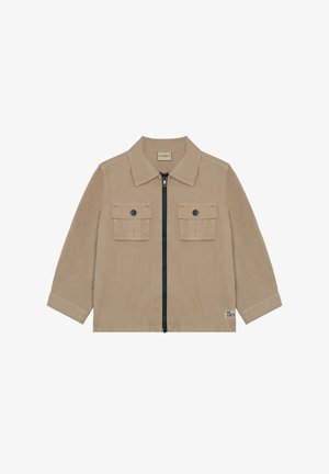 Beige jakke med krave, lynlås foran og to brystlommer. Har kontrasterende navy lynlås og lille mærkedetalje på kanten.