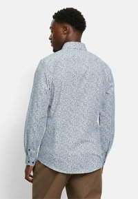 Chemise à manches longues de couleur bleu clair avec un motif cachemire, dotée d'un col pointu et de poignets à boutons. Tissu lisse et coupe ajustée.