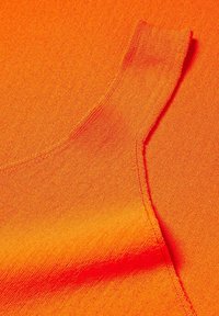 Tissu orange vif avec une surface texturée. Présente une sangle d'épaule et des bords lisses, mettant en avant un design sans couture.