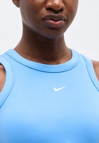 Κοντινό πλάνο ενός ατόμου που φοράει αμάνικο τοπ Nike ανοιχτού μπλε χρώματος με λογότυπο Nike swoosh σε λευκό στο στήθος.