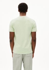 Lichtgroene T-shirt met korte mouwen van zachte katoen. Voorzien van een ronde halslijn en een comfortabele pasvorm. Gepaarde met lichtgrijze broek met zakken.