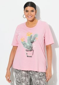Camiseta de manga corta rosa claro con un gráfico de cactus con flores amarillas y el texto "NO ME TOQUES" debajo. Material suave, ajuste relajado.
