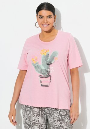 T-shirt rose pâle à manches courtes avec un motif de cactus et des fleurs jaunes, accompagné du texte "NE ME TOUCHE PAS" en dessous. Matière douce, coupe décontractée.