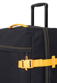 Musta kangaslaukku keltaisilla yksityiskohdilla, jossa on vetokahva, säädettävä hihna soljella ja keltaiset ompelu- sekä yksityiskohdat.