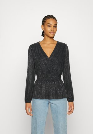Blusa preta de manga longa com decote em V, design pregueado e brilho subtil. Cintura elástica com um corte descontraído, combinada com jeans azul claro.