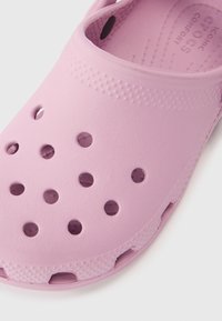 Rozā viegls klogs ar ventilācijas caurumiem, teksturētu virsmu un izliekts malām, izgatavots no sintētiska materiāla ērtībai un izturībai.