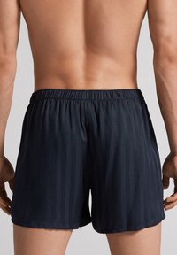Marina blå badshorts i lättviktstyg, med ett subtilt vertikalt randmönster och resårmidja för komfort.