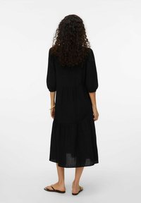 Svart linneklänning med trekvartsärmar, lagerdesign och längd under knäet. Buren med platta sandaler, minimal detalj.