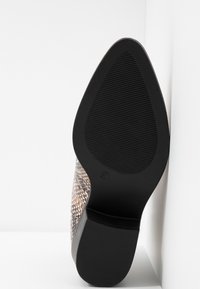 Semelle d'une chaussure à bout pointu avec une semelle en caoutchouc texturé et un talon bloc, montrant le dessus en imprimé serpent sur fond blanc.