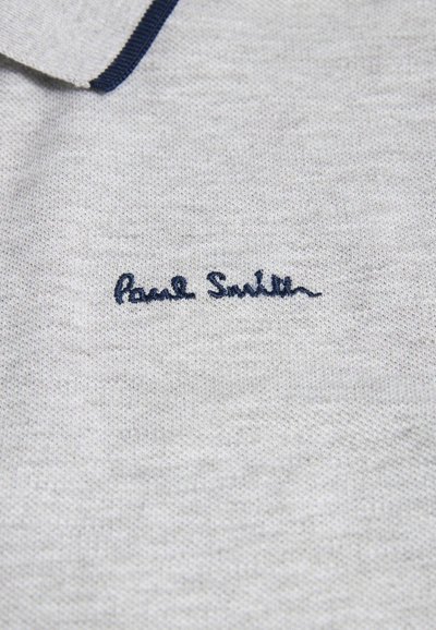 Világosszürke pólóing, kötött textúrával, sötétkék gallérral. Sötétkék hímzett "Paul Smith" logóval rendelkezik.
