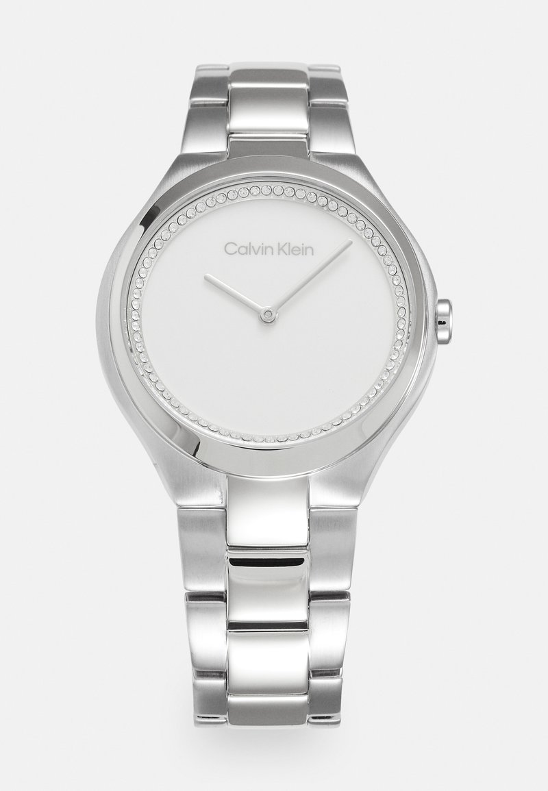 Reloj de acero inoxidable plateado con una esfera redonda minimalista, dial blanco y acentos de cristal alrededor del bisel. Cuenta con una pulsera metálica vinculada.