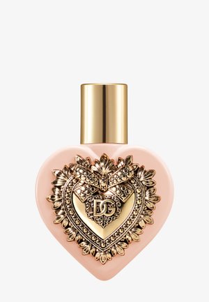 Bottiglia di profumo rosa a forma di cuore con decorazioni ornate dorate a fiori e fiocco, logo DG sul davanti e tappo cilindrico dorato.