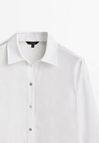 Camicia bianca a maniche lunghe con colletto a punta, realizzata in tessuto leggero, esposta su uno sfondo bianco uniforme.