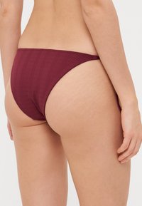 Burgundy ribbed bikini bottom with a low-rise cut, showcasing a textured fabric and minimal coverage design.