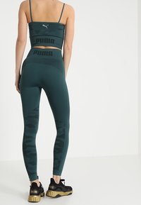 Komprese crop top a legíny v tmavě zelené barvě, s ribbed texturou, logo akcenty a bočními panely v maskáčovém vzoru.