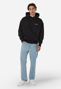 Μαύρη βαμβακερή φόρμα με τσέπη καγκουρό, που διαθέτει λευκό λογότυπο. Συνδυασμένη με ανοιχτό μπλε τζιν και λευκά αθλητικά παπούτσια. Ανεπίσημη εφαρμογή και στυλ.