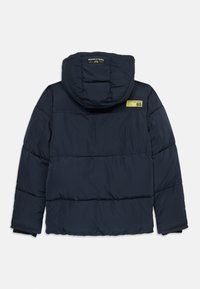Veste matelassée bleu marine avec capuche, ornée d'une étiquette jaune "Scotch & Soda 85" sur l'épaule arrière et de panneaux horizontaux cousus.