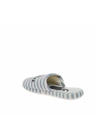 Zapatilla de tela a rayas en azul claro y gris, con punta redondeada y parte trasera abierta. Logo negro destacado en la parte frontal. Textura suave.