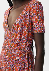 Floral Wickelkleid mit kurzen Ärmeln, auf einem schwarzen Hintergrund mit lebhaften roten, lila und gelben Blumen. An der Taille gebunden.