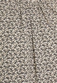 Tissu à motifs présentant de petites fleurs noires et marron sur un fond crème, avec des plis pour une texture et une dimension supplémentaires.