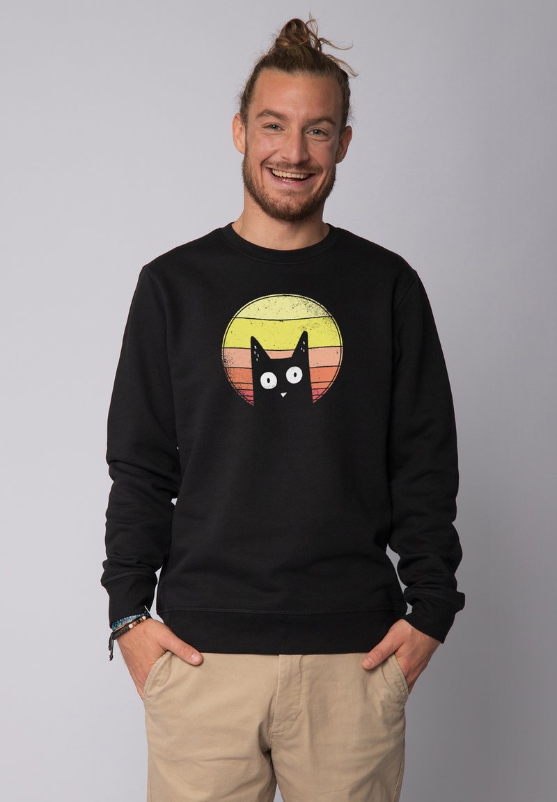 Zwarte sweatshirt van katoen met een ronde afbeelding van een zwarte kat tegen een zonsondergangsverloop van geel, oranje en rood.