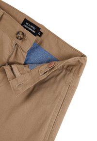 Pantalons en coton beige avec fermeture éclair et bouton. L'intérieur présente une doublure en denim bleu. Comprend des passants de ceinture et des détails de couture subtils.