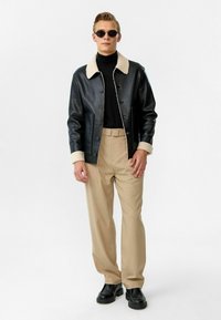 Zwarte leren jack met een crèmekleurige shearling kraag, gecombineerd met een zwarte coltrui, beige broek en zwarte laarzen. Eenvoudig ontwerp, rechte snit.