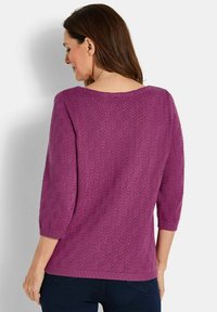 Lila gestrickter Pullover mit Dreiviertelärmeln und strukturiertem Muster, mit einem weiten Halsausschnitt und geripptem Saum, kombiniert mit dunklen Jeans.