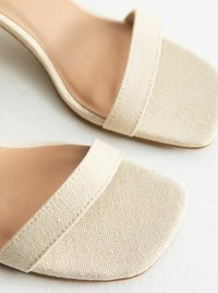 Beige tygtofflor med fyrkantiga tår, som har breda kanvasremmar och en slät beige inredning. Texturerat yttermaterial.
