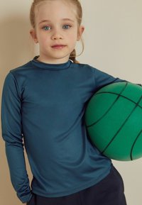 Långärmad, teal träningsskjorta av mjukt tyg, ihop med en grön basketboll med svarta horisontella linjer.