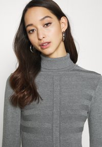 Grå turtleneck genser med ribbestruktur og horisontale stripe mønstre. Har en tettsittende design og mykt strikket materiale.