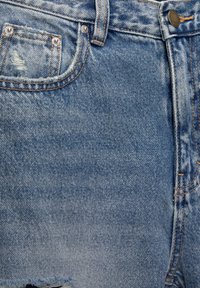 Denimshorts i ljusblått med en urtvättad yta. Har en framficka, sömdetaljer i orange och slitna nederkanter.