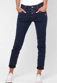 Mörkblå slim-fit byxor i denim med femknapps-stängning, snedställda fickor och uppvikta benslut. Bärs med vita sneakers.